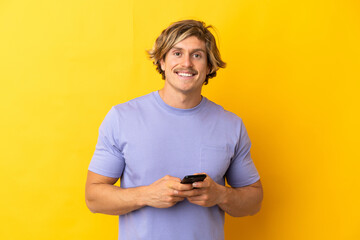 Handsome blonde man isolated on yellow background sending a message with the mobile