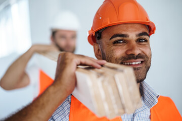 Two young men builders carrying wood planks on construction site, close up