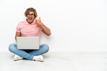 Young caucasian man sitting on the floor with his laptop isolated on white background making phone gesture. Call me back sign