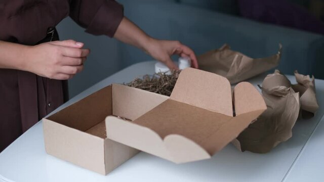 woman is packing jars of cosmetics in a box to send a parcel through a delivery service.