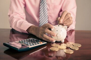 The hand of a businessman puts coins in a piggy bank, saves money with coins, steps into a successful growth business, and saves for retirement concept