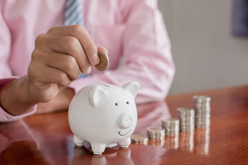 The hand of a businessman puts coins in a piggy bank, saves money with coins, steps into a...