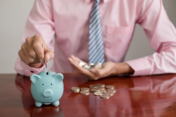 The hand of a businessman puts coins in a piggy bank, saves money with coins, steps into a...