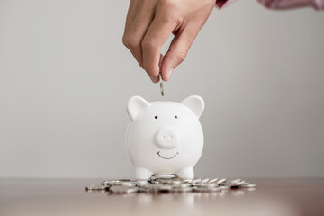 The hand of a businessman puts coins in a piggy bank, saves money with coins, steps into a...