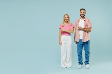 Full body young cool couple two friends family man woman in casual clothes point index finger aside on workspace area mock up copy space together isolated on pastel plain light blue background studio.