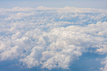 White cumulus clouds over snowy mountains. Above the clouds, view from the plane.