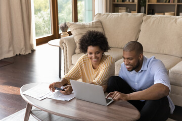Happy millennial african american family couple analyzing financial paper documents, managing household budget or paying for services in e-banking computer app, enjoying calculating expenses at home. - Powered by Adobe