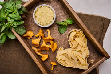 Raw ingredients for making Italian pasta pappardelle with mushrooms chanterelles and cheese in rustic wooden tray on linen napkin, top view flat lay