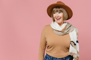 Traveler tourist surprised fun mature elderly lady woman 55 years old wears brown shirt hat scarf look aside isolated on plain pastel light pink background studio portrait. Air flight journey concept.