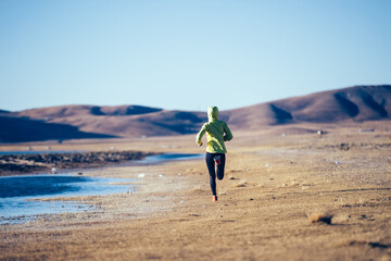 Woman trail runner running on winter high altitude lakeside