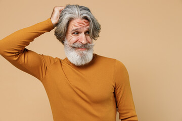 Elderly gray-haired mustache bearded puzzled man 50s in mustard yellow turtleneck shirt scratch...