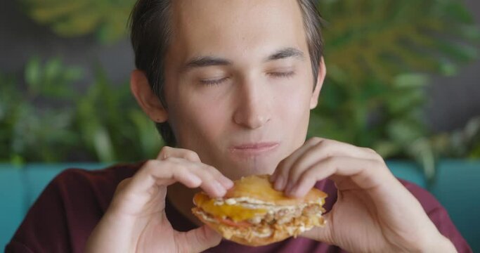 Close up shot of handsome men are eating burger in fast food restaurant. People eat unhealthy meal. Getting satisfaction from unhealthy food. Junk food, modern life concet. Front view, slow motion