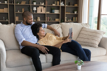Happy bonding young married mixed race family couple using digital tablet, planning travel booking...