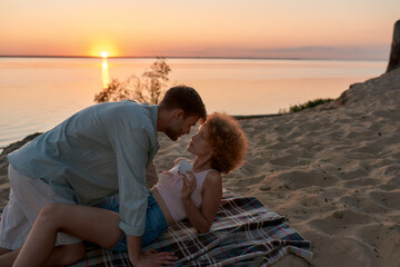 Beautiful young couple lying on the beach at sunset, ready for making love. Woman is holding a...