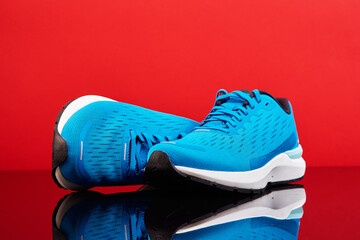 Blue running sneakers on red background. Pair of sport male shoes for fitness with reflection,...