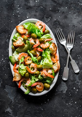 Delicious salad with shrimp, crispy iceberg, crackers and olives on a dark background, top view
