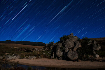 Obraz premium Star trail over creek and rocky outcrop with moonlight illuminating landscape