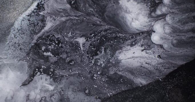 Black white flowing paint background, close-up. Abstract alcohol ink mixed with silver glitter. Black liquid, white color moving. Liquid marble texture. Inkscapes dark gray shimmer surface in motion 