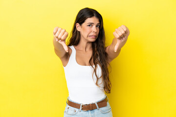 Young caucasian woman isolated on yellow background showing thumb down with two hands