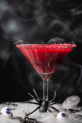 Close-up of cherry cocktail for Halloween with smoke, on table with spiders and eyes, selective focus, black background, vertical