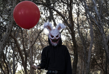 Halloween model with rabbit mask and red balloon in an enchanted forest.