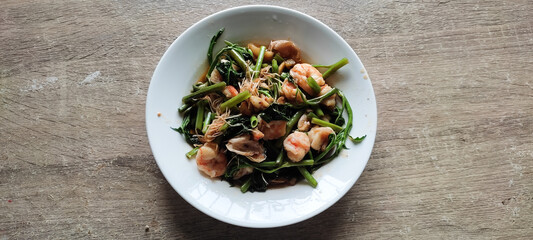 Stir fried morning glory with shrimp in a white plate.