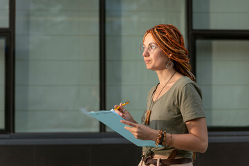 Young beautiful girl with red dreadlocks listens and records information. Outdoor training. Woman...