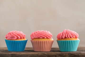 Delicious vanilla mousxes with pink cream. Three homemade muffins on wooden. Copy space. Birthday cupcake on light background.