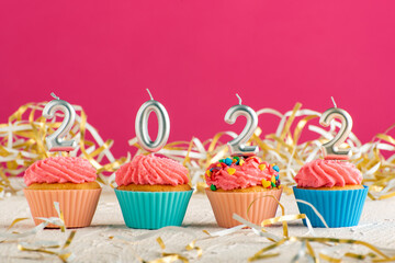 Festive cupcakes and candles in form of numbers 2022 on pink background. Concept of New year.