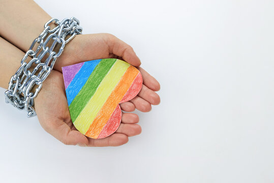 Paper heart painted in LGBT colors in the hands of a woman tied in chains.