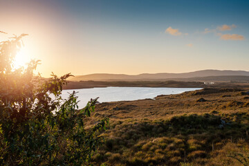 Small lake with blue water and wild fields. Beautiful sun rise scene in Connemara, county Galway, Ireland. Warm and cool tones. Haze over mountains in the background.