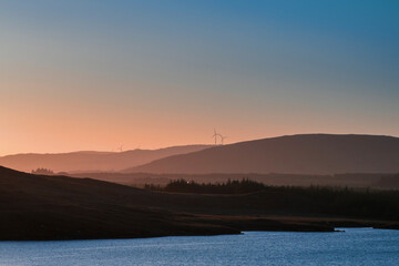 Small lake with blue water and wild fields. Beautiful sun rise scene in Connemara, county Galway, Ireland. Warm and cool tones. Haze over mountains in the background.