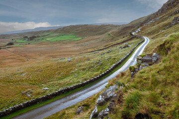 Small narrow country road on a hill by a traditional stone wall with beautiful nature scene. West of Ireland. Irish landscape. Green grass. Fog in the background. Transportation industry.