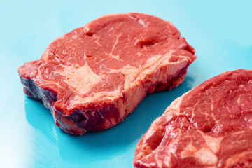 Fresh juicy rib eye steak on blue surface. Top quality fresh meat. Butcher craft product and meat industry. Rich red color and marbling. Premium cut.