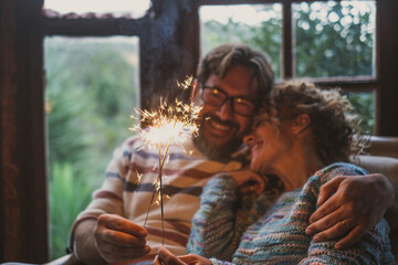 Couple celebrate alone at home with smile and fire sparkler sitting on the couch qieh outdoor...