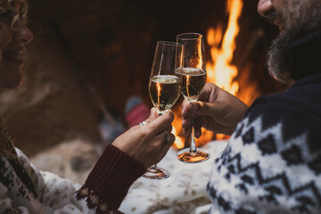 Close up of couple clinking glasses with champagne or wine together at home in front of a warm fireplace. Romantic celebration christmas or new year man and woman. People indoor © simona