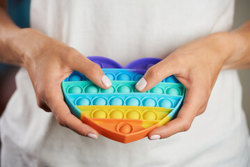 Close-up photo of a toy "Pop it" in the shape of a heart in the hands of a girl