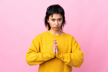 Young Uruguayan woman over isolated pink background keeps palm together. Person asks for something