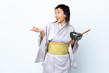 Young woman wearing kimono holding a bowl of noodles over isolated white background with surprise facial expression
