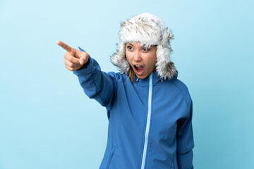 Young Uruguayan girl with winter hat isolated on blue background pointing away