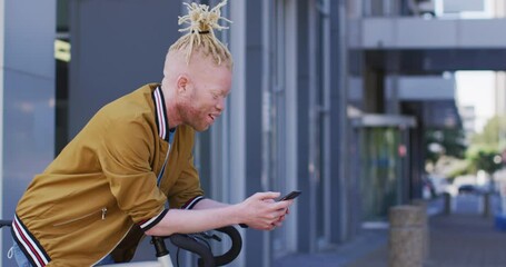 Happy albino african american man with dreadlocks on bike using smartphone - Powered by Adobe