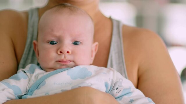Newborn baby in her mother's arms. Mom holds the baby in her arms. The child looks into the camera.  Infant with blue eyes.