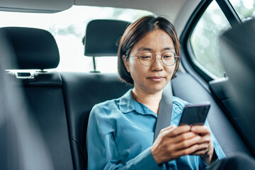 Asian businesswoman on the backseat of a car, using smart phone