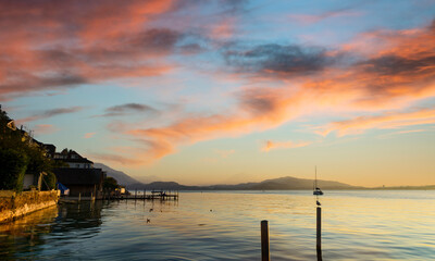 View of Lake Zugersee from the Swiss town of Zug, at sunset and calm with the cloudy sky tinged by the light of the setting sun.