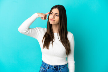 Young caucasian woman isolated on blue background making the gesture of madness putting finger on...