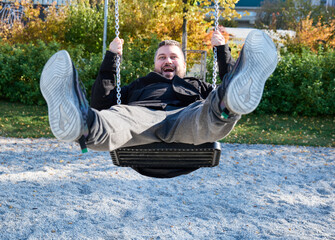 adult bearded man rides a child's swing and laughs