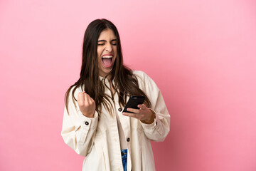 Young caucasian woman isolated on pink background with phone in victory position