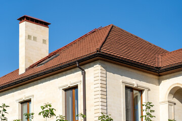 Corner of house with new brown metal tile roof and rain gutter. Metallic Guttering System, Guttering and Drainage Pipe Exterior