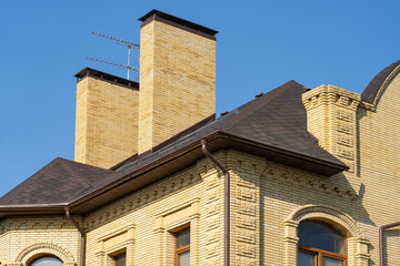 house with drainage system on metal roof. Сhimney pipes is finished externally with natural stone. Roof gutter pipeline system. House rain gutter with holders and downspout pipe
