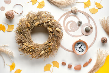 Autumn time background. Dried grass wreath, wood alarm clock, off white table with ginko leaves,...